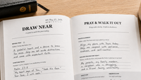 Open notebook with writing on a wooden surface with a mug and pen.
